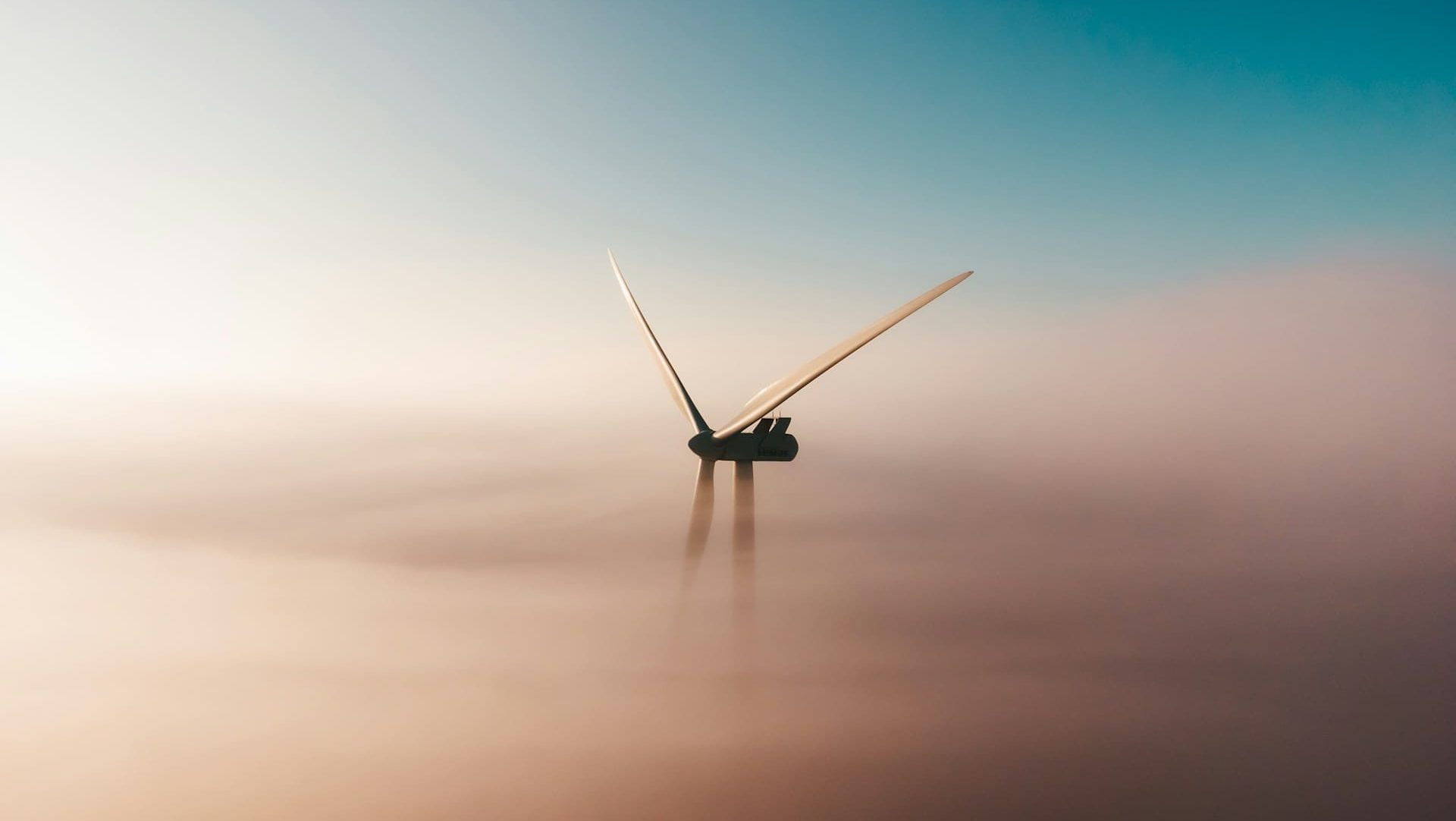 Windkraftanlage ragt aus einer Nebelschicht in den Himmel – Symbol für den Übergang zu einer klimafreundlichen und emissionsarmen Wirtschaft.